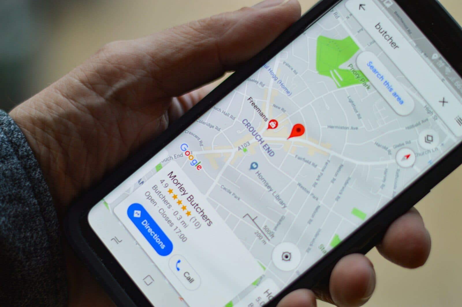 A hand holding a phone that shows a map search with a location pin