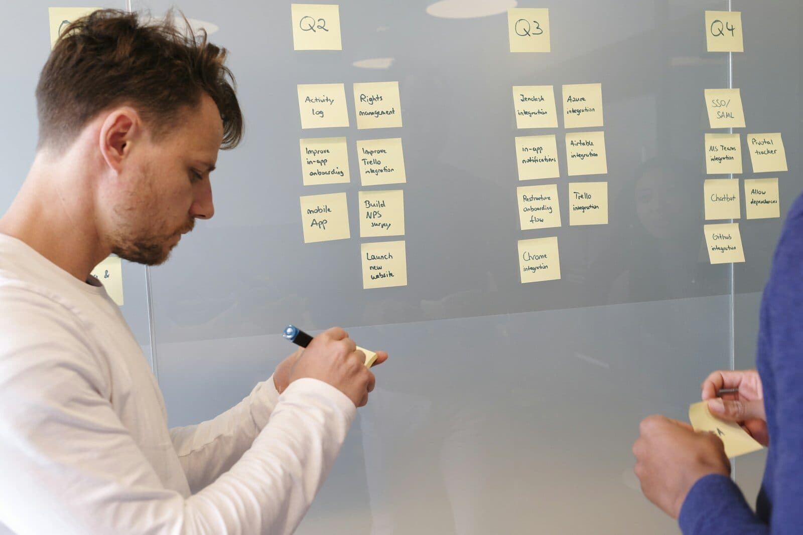 A man writing on a glass board covered in notes
