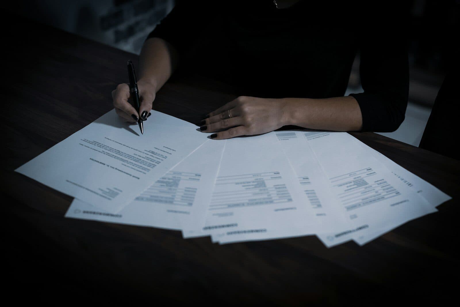 A person reviewing a spread of printed documents at a dark table