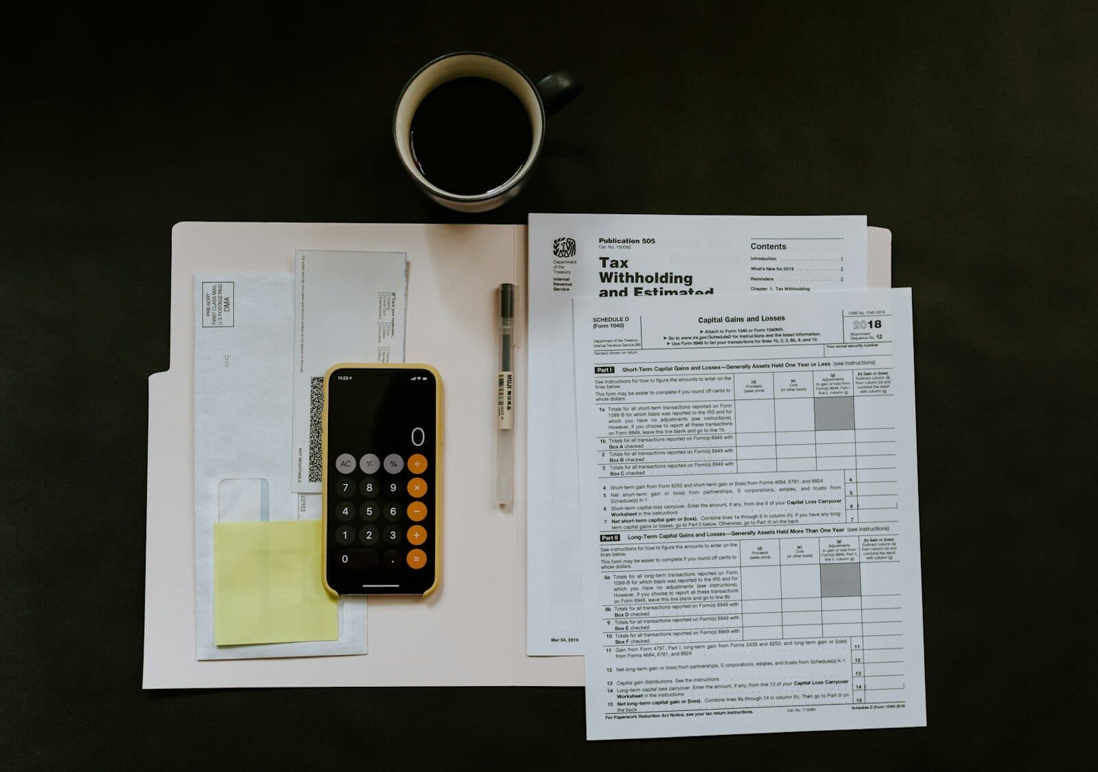 Tax forms, a calculator and a pen on a desk beside a coffee cup