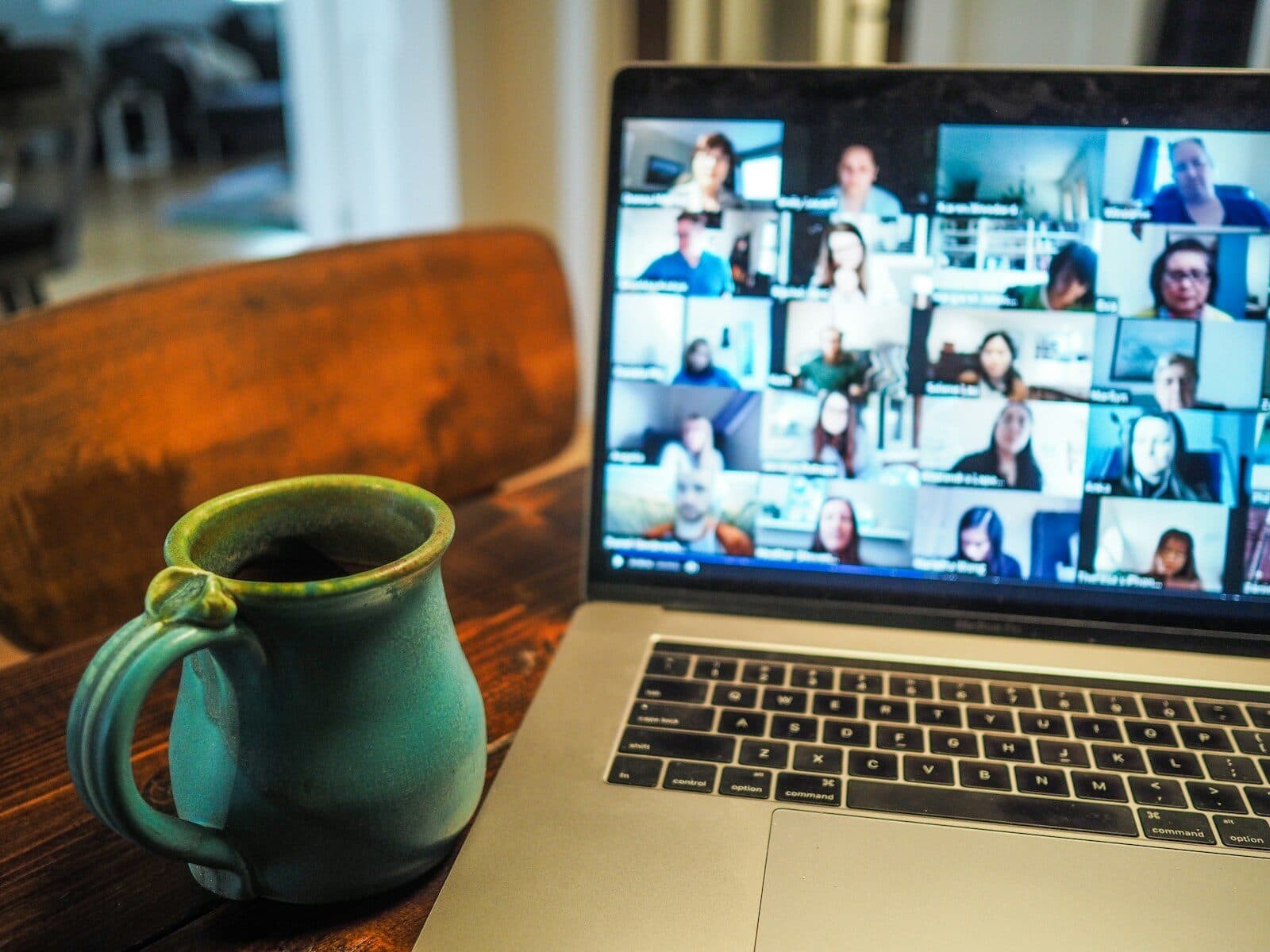 A laptop showing a video meeting with many participants, next to a mug