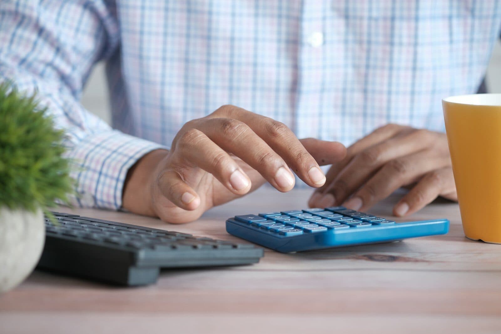 Hands working a calculator beside a keyboard and a coffee mug